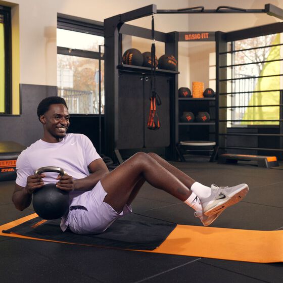 Un membre r&eacute;alise un Russian twist avec une kettlebell sur un tapis dans l'espace d'entra&icirc;nement fonctionnel chez Basic-Fit.