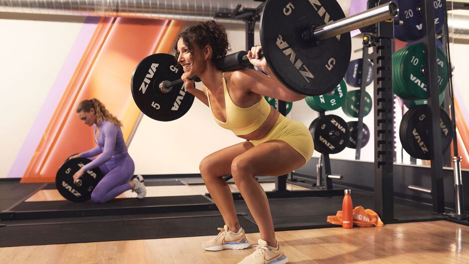 Personal trainer begeleidt een vrouw tijdens een lunge oefening in een functionele trainingsruimte in een Basic-Fit gym