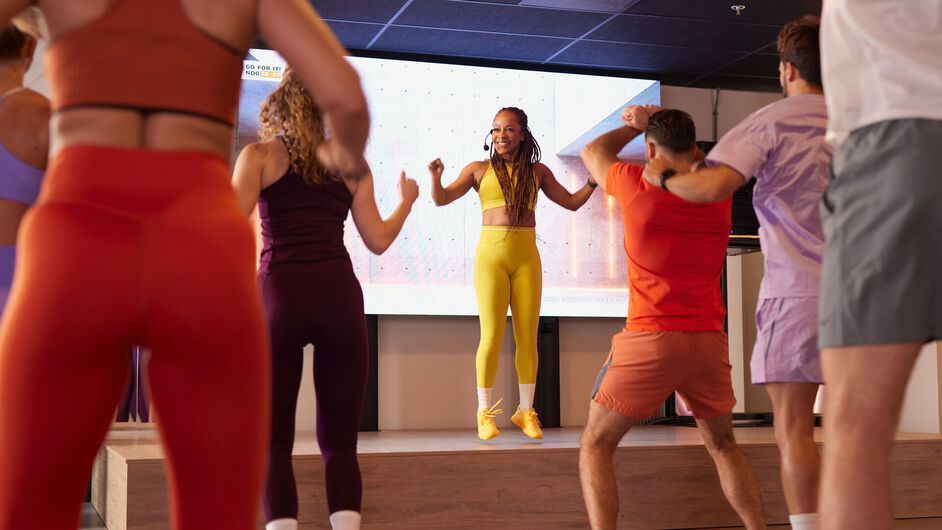 Les participants prennent part &agrave; un cours de fat burn cardio et encha&icirc;nent les mouvements ensemble en suivant le coach &agrave; l&rsquo;avant de la salle.