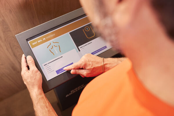 Un membre utilise l'&eacute;cran tactile du Body Analyzer Basic-Fit pour d&eacute;marrer une analyse de la composition corporelle.