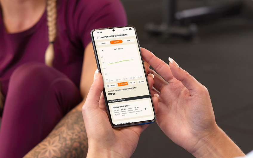 Membre consultant l'&eacute;volution de sa masse musculaire dans l'application Basic-Fit pendant son entra&icirc;nement.