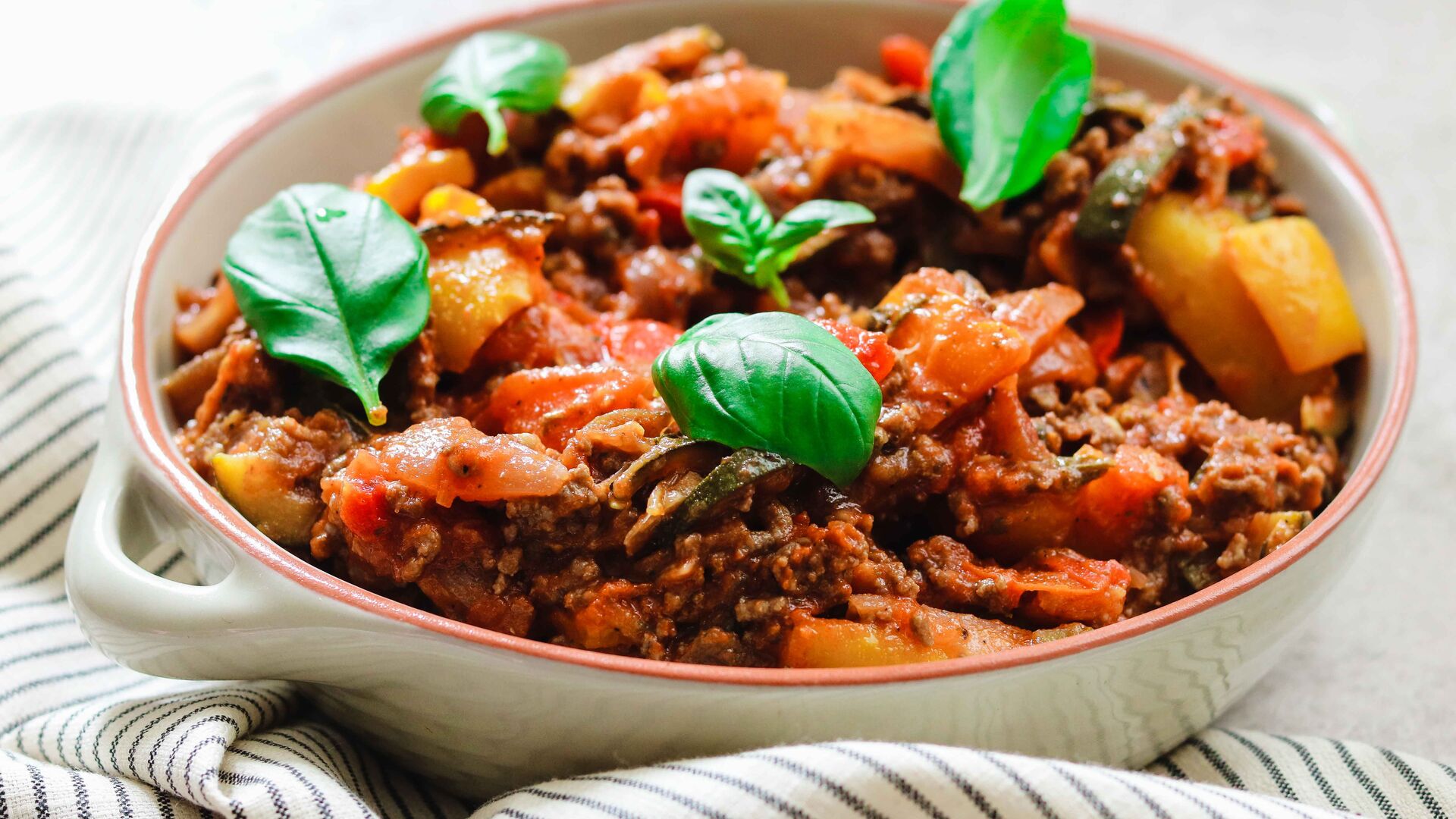 Plat de ratatouille à base de viande et de légumes, garni de feuilles de basilic frais.