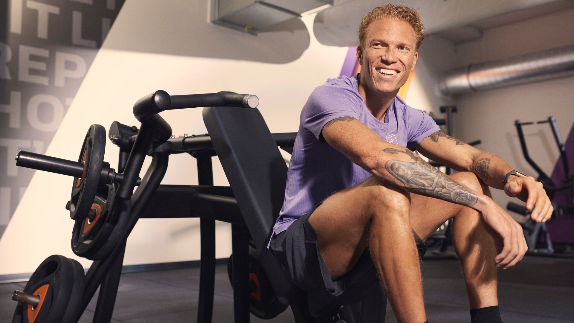 Homme assis sur une machine de musculation en salle de sport, souriant après son entraînement.