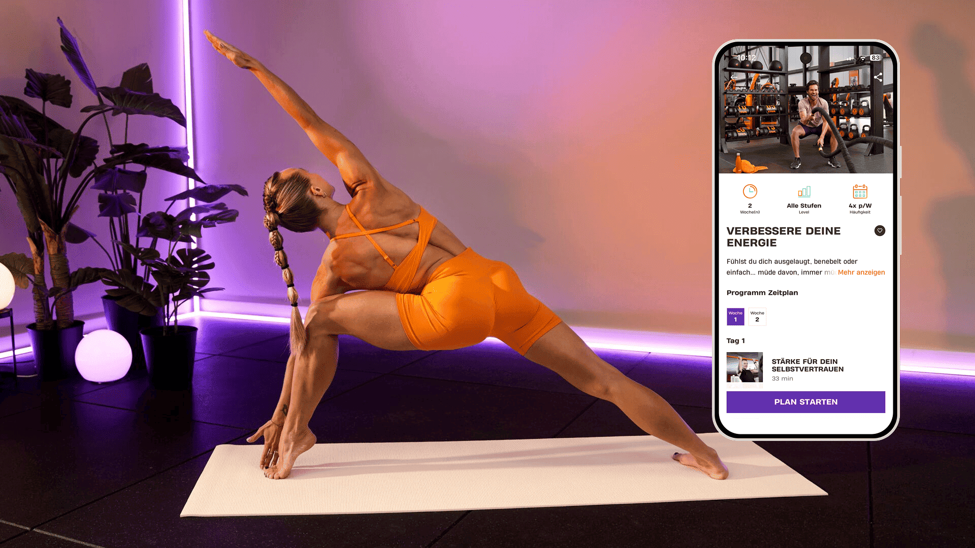 Eine Frau macht eine tiefe Dehnübung in einer Yoga-Pose auf einer Matte in einem Raum mit violetter Beleuchtung und tropischen Pflanzen. Sie trägt leuchtend orangefarbene Sportkleidung. Neben ihr zeigt ein Smartphone das Basic-Fit-Programm „Verbessere deine Energie“ mit Trainings für Kraft und Selbstvertrauen.