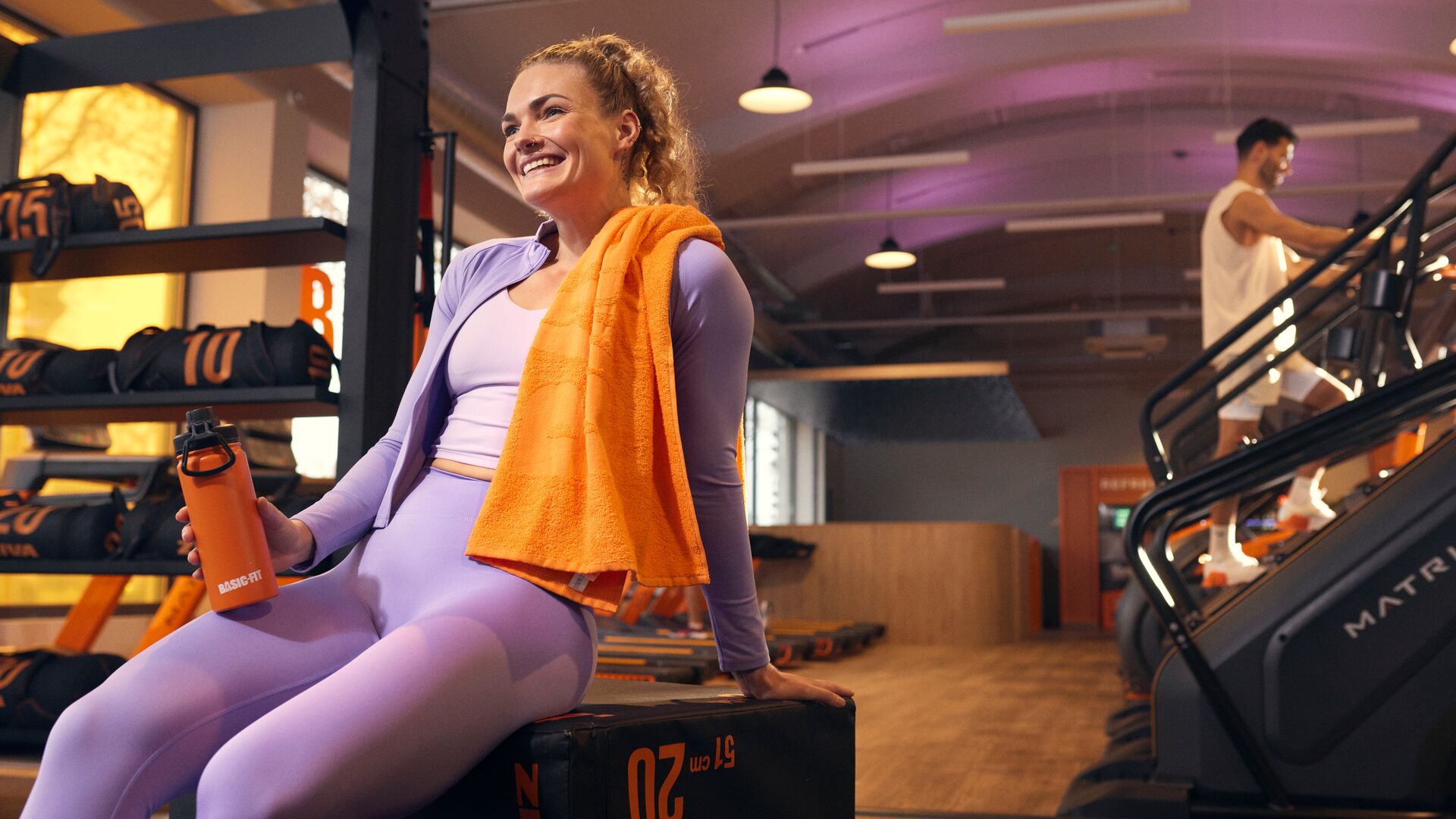 Vrouw rust uit na haar workout in de sportschool terwijl een man traint op een stair climber
